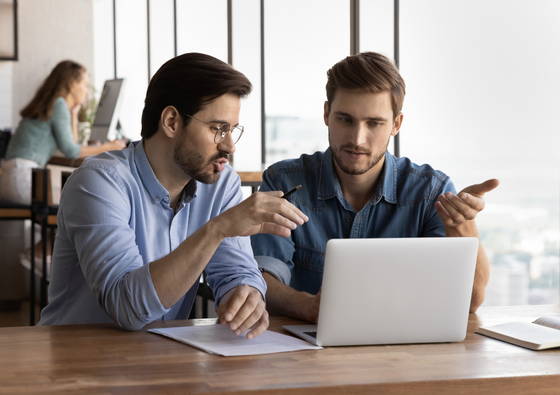 two businessmen speak towards laptop, appearing to be on a call