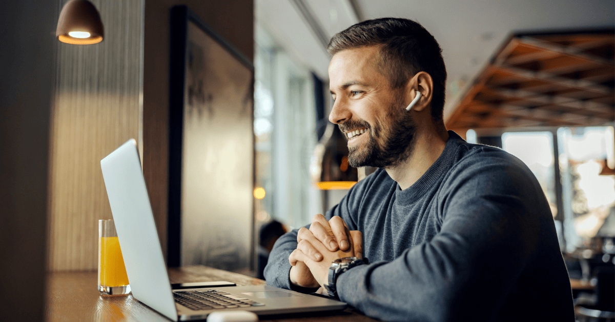 a man sits in front of a laptop with earphones in, on a video call